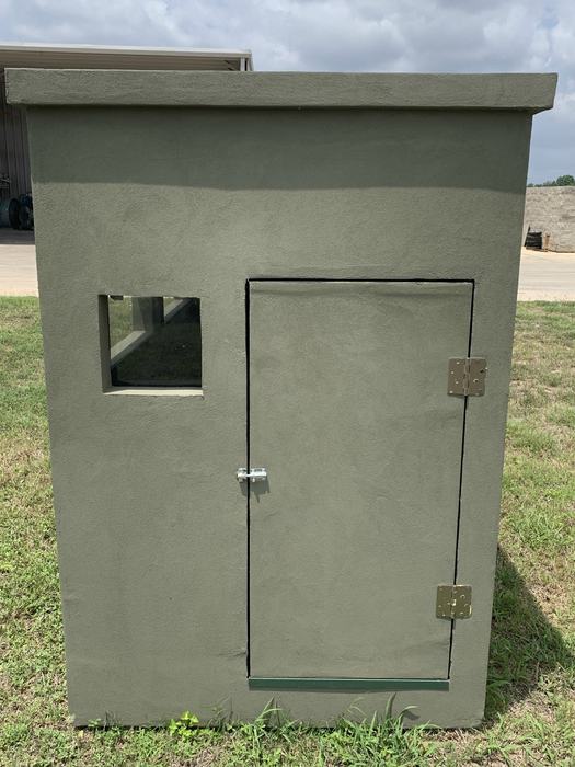 Exterior of a 4x8 insulated deer blind, showing the textured three-layer stucco finish and hinged door